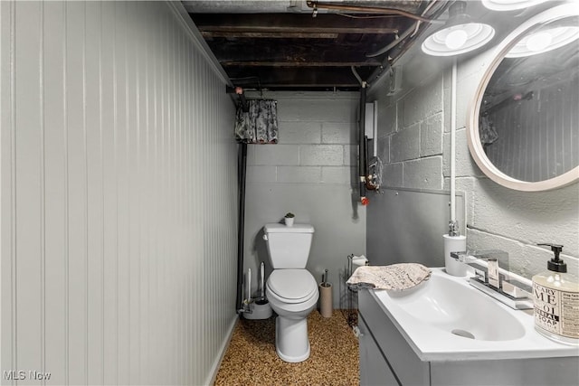 half bathroom featuring speckled floor, vanity, toilet, and concrete block wall