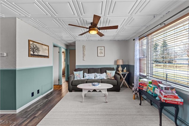 living area with wood finished floors, a wainscoted wall, an ornate ceiling, and ceiling fan