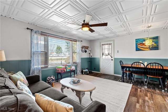 living room with ceiling fan, a wainscoted wall, an ornate ceiling, and wood finished floors