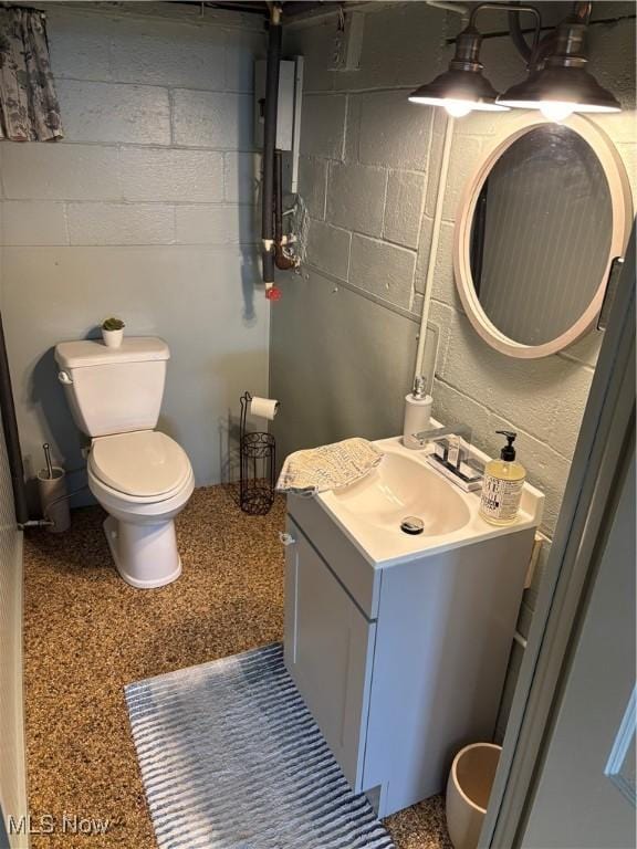 bathroom featuring vanity, toilet, and concrete block wall