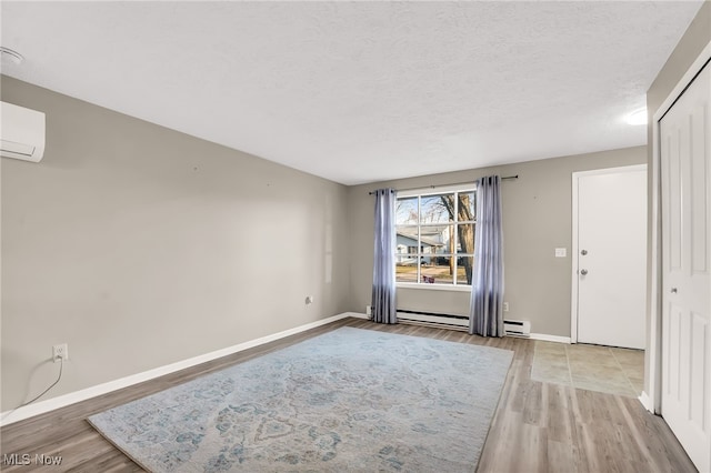 unfurnished room with a baseboard heating unit, baseboards, light wood-style flooring, a textured ceiling, and a wall mounted AC