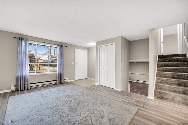 unfurnished living room featuring stairway, wood finished floors, and a baseboard heating unit