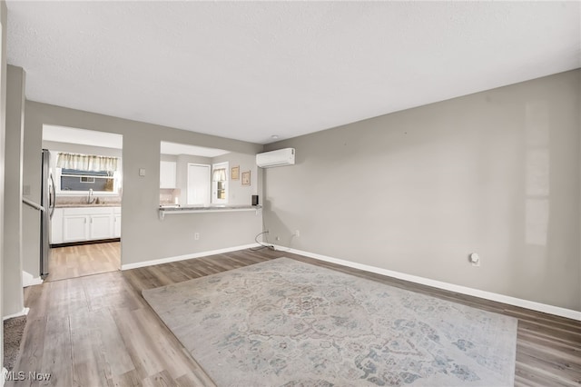 unfurnished living room with baseboards, a wall unit AC, wood finished floors, a textured ceiling, and a sink