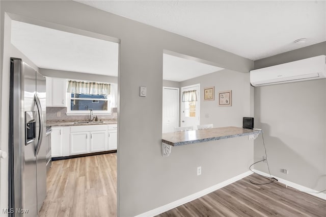 kitchen with a wall unit AC, light wood finished floors, stainless steel fridge with ice dispenser, a sink, and white cabinetry