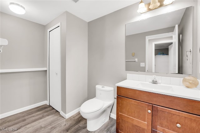 half bathroom featuring toilet, vanity, baseboards, and wood finished floors