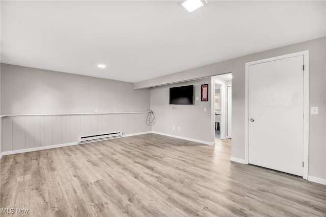 interior space featuring a baseboard heating unit, a wainscoted wall, and light wood finished floors