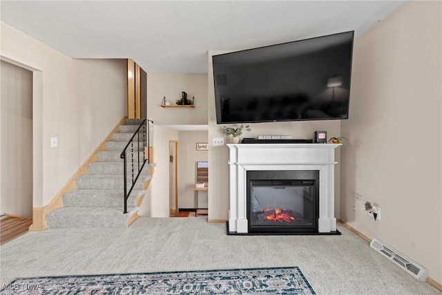 living room with carpet, baseboards, visible vents, stairs, and a glass covered fireplace