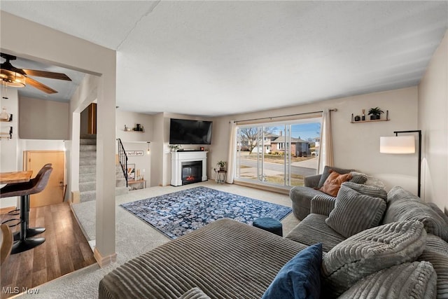 living room featuring a glass covered fireplace, stairway, and a ceiling fan