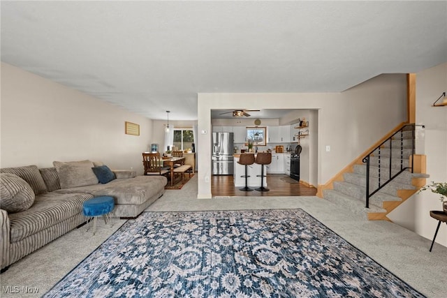 living area with carpet, ceiling fan, and stairs