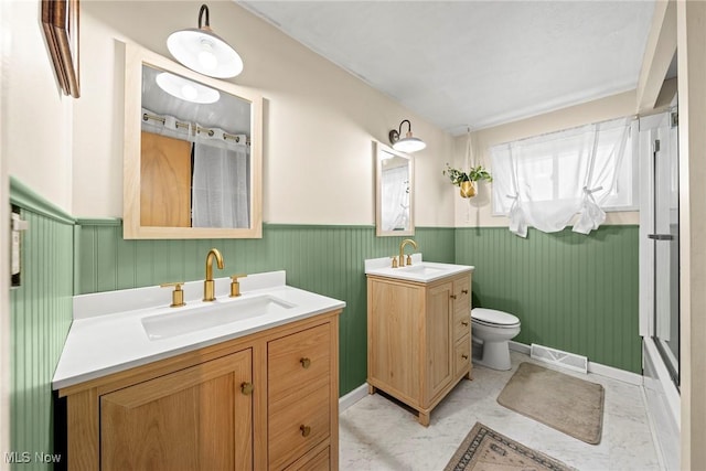 bathroom with visible vents, wainscoting, two vanities, and a sink