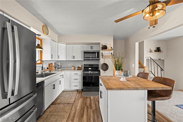 kitchen featuring a kitchen bar, butcher block countertops, black appliances, a sink, and dark wood finished floors