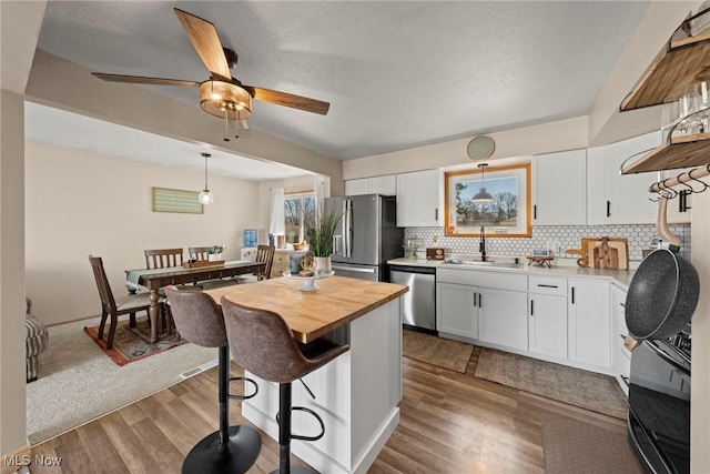 kitchen featuring a breakfast bar, a sink, stainless steel appliances, white cabinets, and wood counters