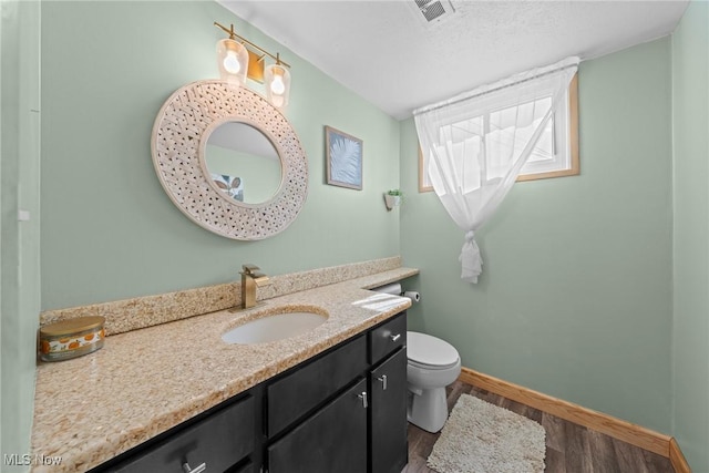 bathroom featuring vanity, wood finished floors, visible vents, baseboards, and toilet