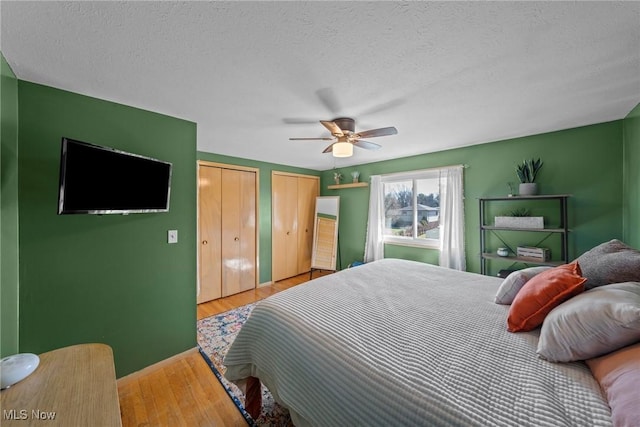 bedroom featuring a textured ceiling, two closets, a ceiling fan, and wood finished floors