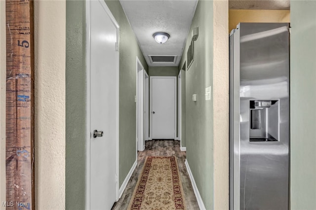 hall with visible vents, baseboards, wood finished floors, a textured wall, and a textured ceiling