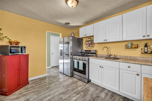 kitchen with white cabinets, light wood-type flooring, appliances with stainless steel finishes, and a sink