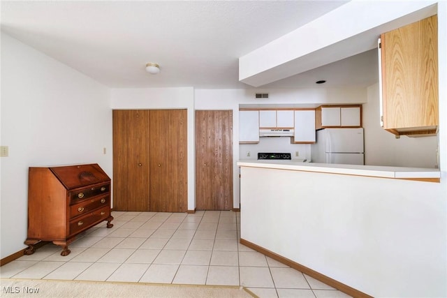 kitchen with visible vents, under cabinet range hood, freestanding refrigerator, a peninsula, and light tile patterned floors