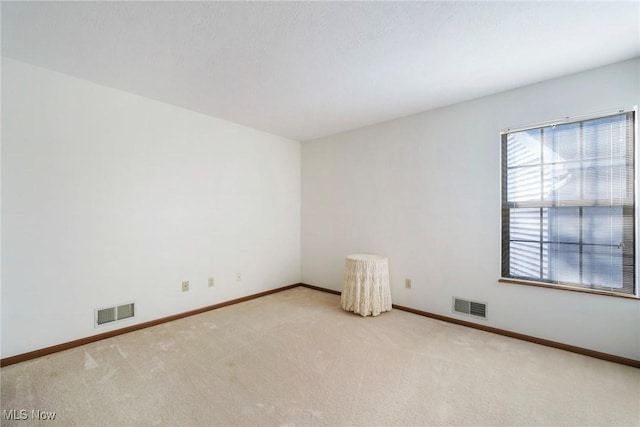 empty room featuring light carpet, visible vents, and baseboards