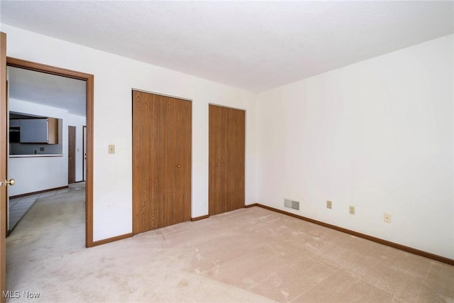 unfurnished bedroom with visible vents, carpet flooring, two closets, and baseboards