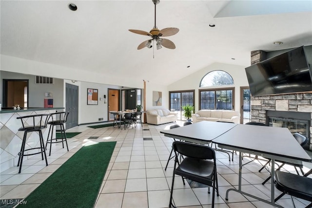 dining room with visible vents, light tile patterned floors, a stone fireplace, high vaulted ceiling, and a ceiling fan