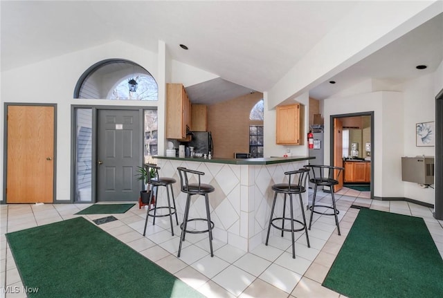 kitchen with light tile patterned floors, dark countertops, a breakfast bar area, and vaulted ceiling