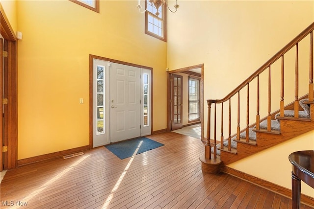 foyer featuring hardwood / wood-style floors, baseboards, visible vents, and a towering ceiling