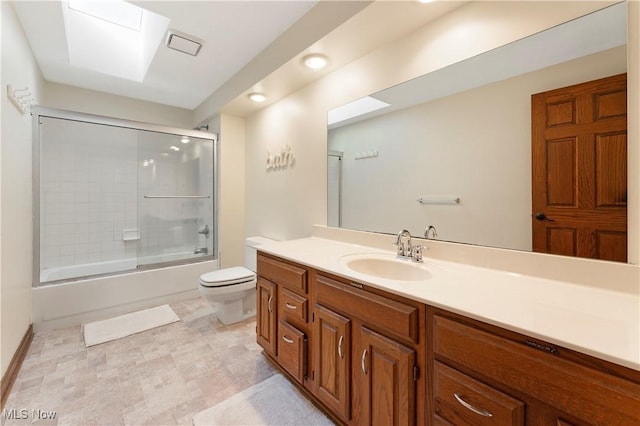 bathroom featuring a skylight, toilet, vanity, and shower / bath combination with glass door