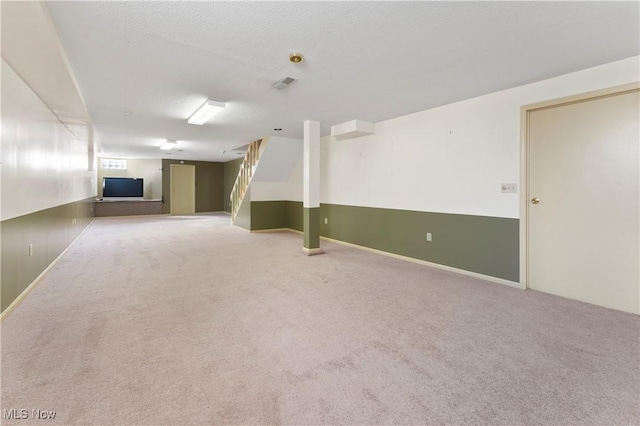 below grade area featuring stairs, visible vents, a textured ceiling, and carpet flooring