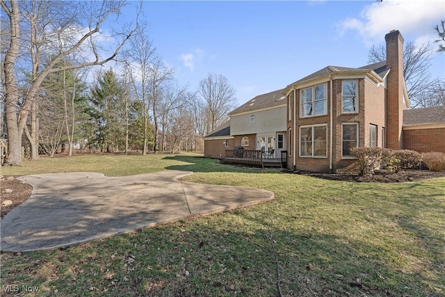 back of house with a deck, a yard, brick siding, and a chimney