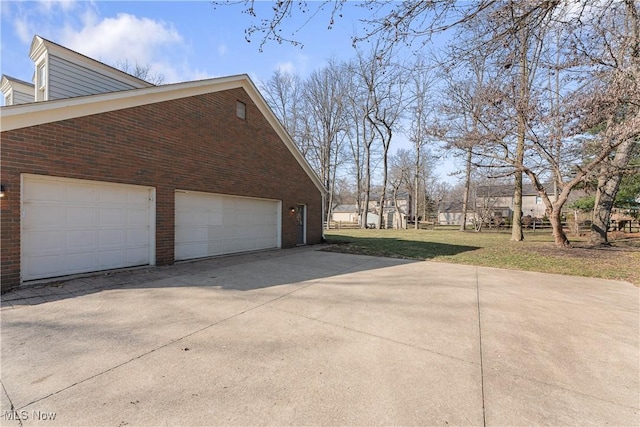 view of side of property featuring brick siding, a lawn, driveway, and a garage