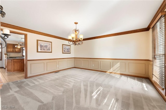 empty room with light carpet, ornamental molding, wainscoting, a decorative wall, and a chandelier