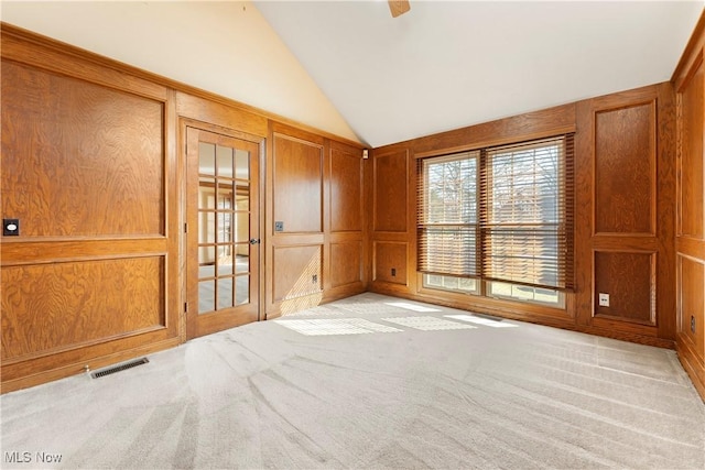 unfurnished room featuring visible vents, wooden walls, a decorative wall, light colored carpet, and vaulted ceiling