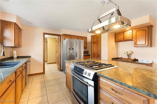 kitchen featuring brown cabinetry, under cabinet range hood, light tile patterned flooring, stainless steel appliances, and a sink