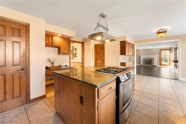 kitchen featuring a fireplace with raised hearth, a center island, gas range, light tile patterned floors, and baseboards