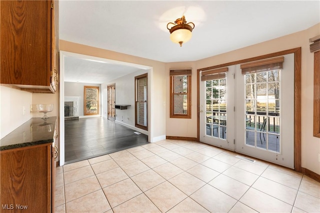 doorway to outside featuring light tile patterned floors, baseboards, and a fireplace with raised hearth