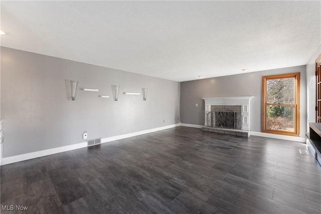 unfurnished living room with dark wood finished floors, a stone fireplace, baseboards, and visible vents