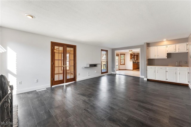 unfurnished living room featuring dark wood-style floors, french doors, baseboards, and a textured ceiling