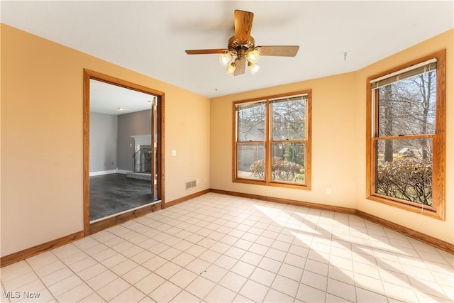 unfurnished room featuring a fireplace with raised hearth, a healthy amount of sunlight, visible vents, and baseboards