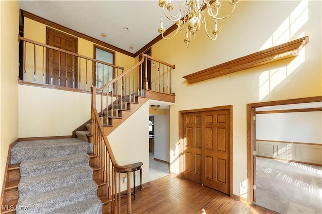 stairway featuring baseboards, crown molding, a towering ceiling, and hardwood / wood-style flooring