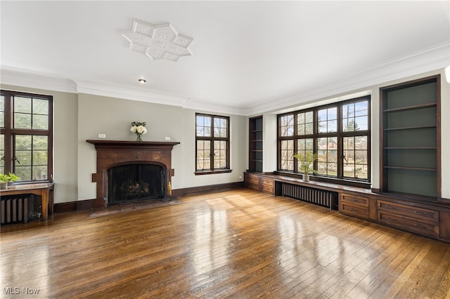 unfurnished living room featuring hardwood / wood-style floors, radiator, ornamental molding, and a fireplace