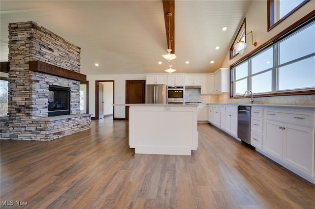 kitchen with a kitchen island, dark wood-type flooring, a fireplace, white cabinets, and stainless steel appliances