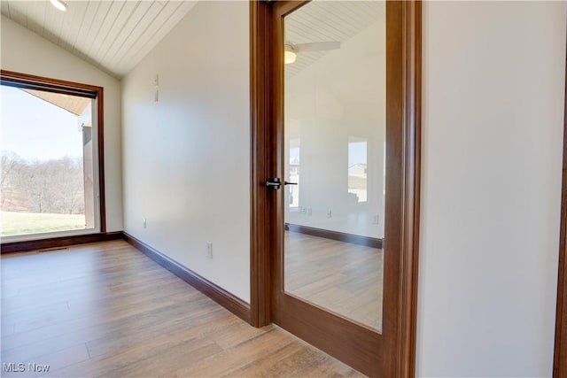 corridor with light wood-type flooring, baseboards, and vaulted ceiling