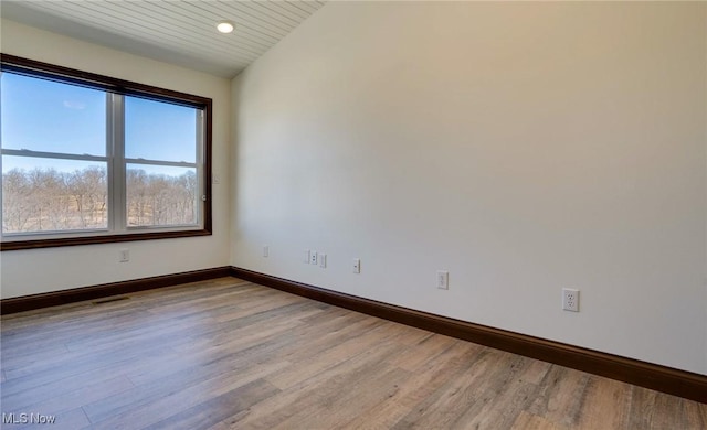 unfurnished room featuring baseboards, light wood-style flooring, and vaulted ceiling