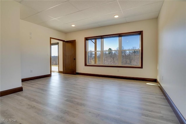 empty room featuring wood finished floors, a healthy amount of sunlight, baseboards, and a drop ceiling