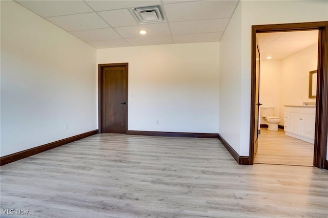 spare room with a drop ceiling, visible vents, baseboards, and light wood finished floors