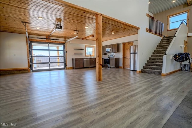 unfurnished living room featuring baseboards, wood ceiling, wood finished floors, and a healthy amount of sunlight