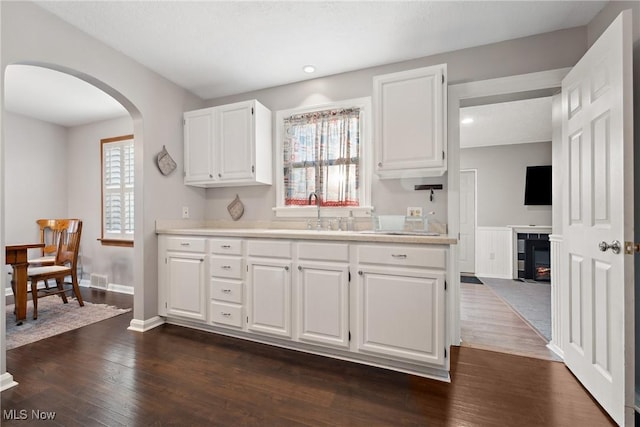 kitchen featuring arched walkways, dark wood-style flooring, a sink, light countertops, and white cabinets