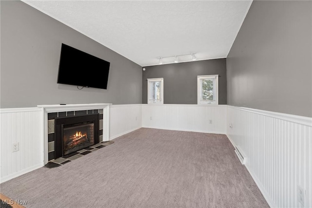 unfurnished living room featuring a wainscoted wall, track lighting, a textured ceiling, carpet floors, and a fireplace