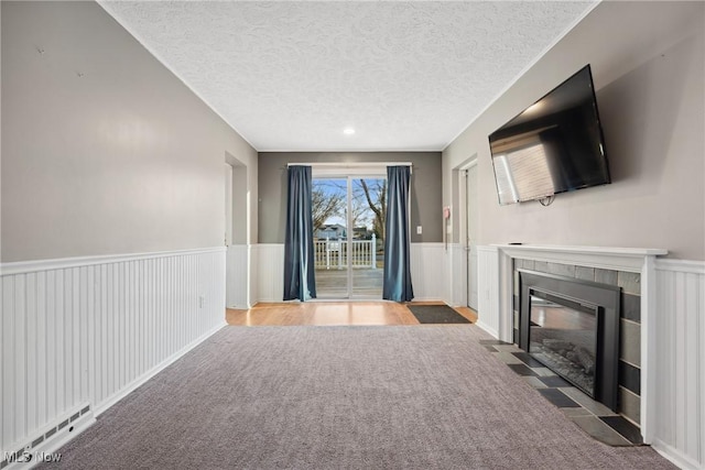 unfurnished living room with a textured ceiling, carpet floors, wainscoting, a fireplace, and baseboard heating