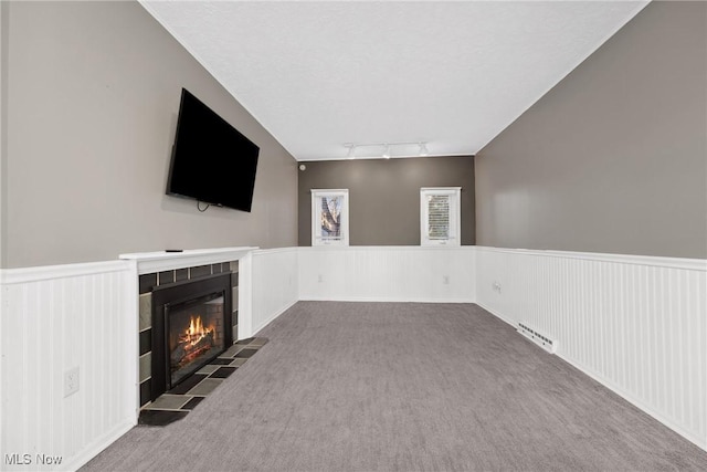 unfurnished living room featuring track lighting, wainscoting, a fireplace, and carpet floors